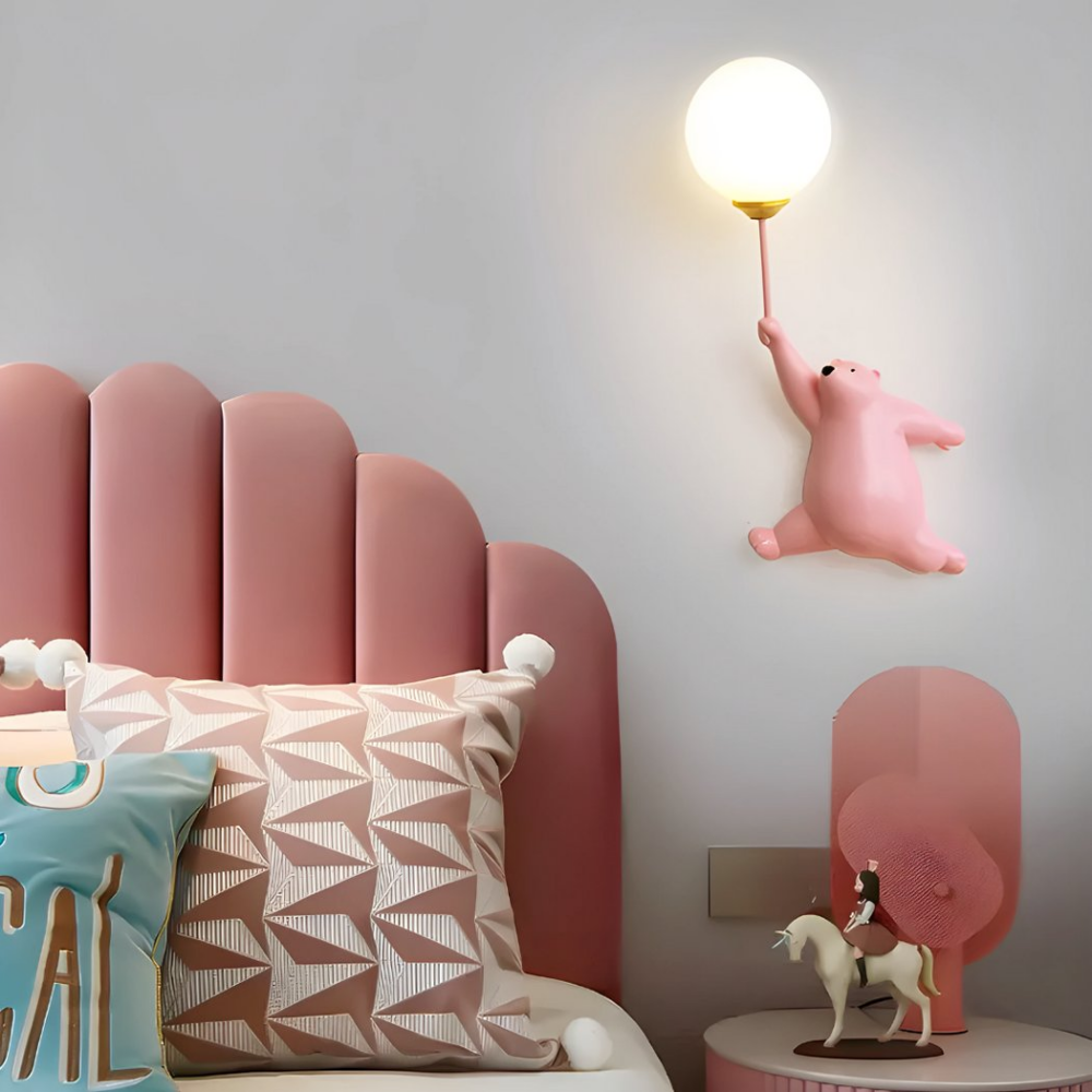 Een roze wandlamp met bal en teddybeer hangt in de slaapkamer van een klein meisje