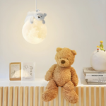 Wandlamp met een beer die op de maan slaapt, hangend in een babykamer en naast een grote teddybeer