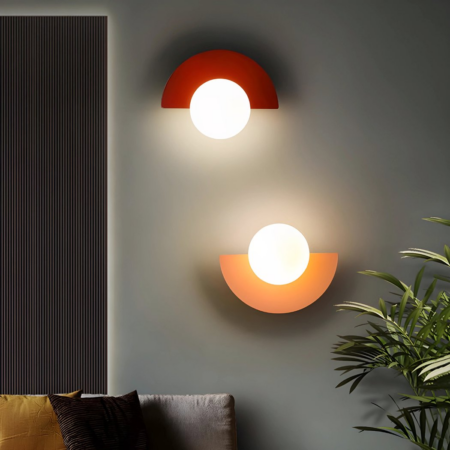 Twee halve maan wandlampen in retrostijl in rood en roze hangen aan een muur naast een kamerplant