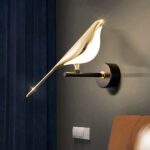 Gouden ekster wandlamp opgehangen aan een zwarte muur naast een hoofdeinde