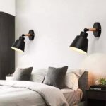 in een slaapkamer staat een bed met grijze kussens en twee zwarte wandlampen op een witte muur