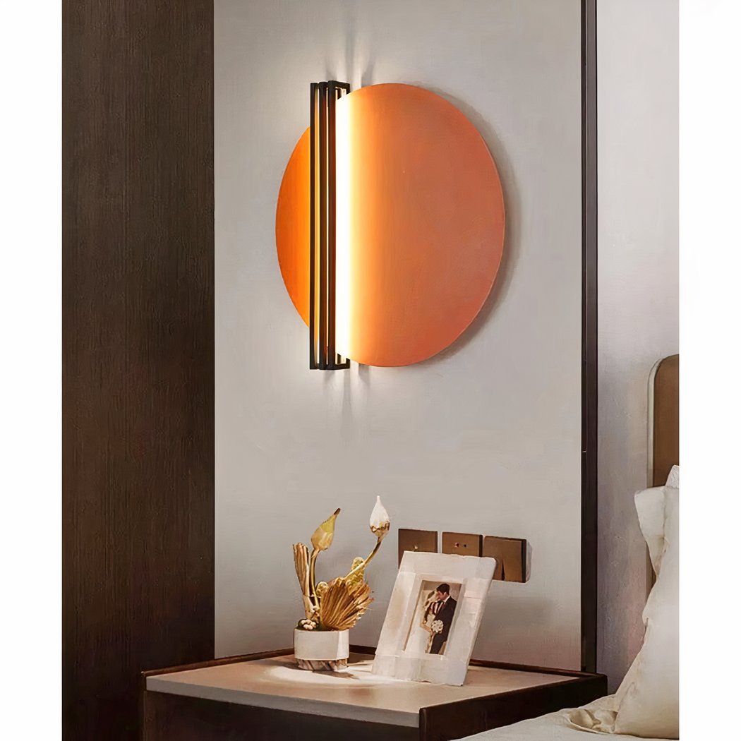 een oranje ronde wandlamp in Scandinavische stijl is te zien boven een nachtkastje in een slaapkamer