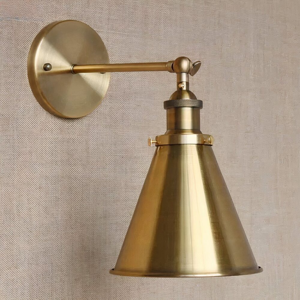 een vergulde metalen wandlamp in industriële stijl is te zien op een lichtbruine muur