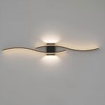 Zwarte wandlamp bevestigd op een grijze muur, in de vorm van 2 golven boven elkaar vastgehouden door een zwarte rechthoekige steun. De golven zijn lichtgevend en het licht komt ook uit de boven- en onderkant van de steun.