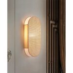 op een donkere muur staat een lichtbruine ovale wandlamp in Japans rietwerk