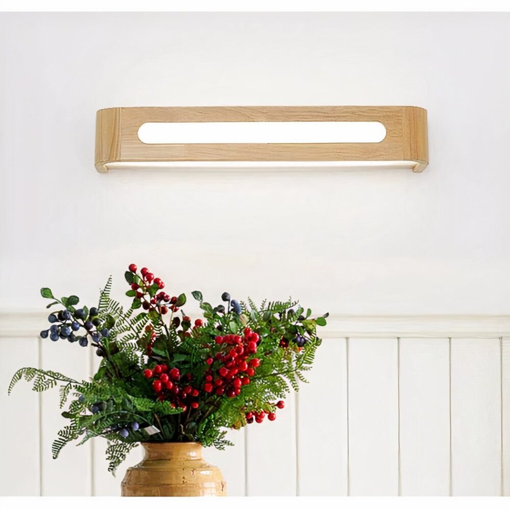 op een witte muur in een huis staat een rechthoekige houten wandlamp voor het interieur waaronder een tafel staat met een vaas en een boeket rode bloemen erin