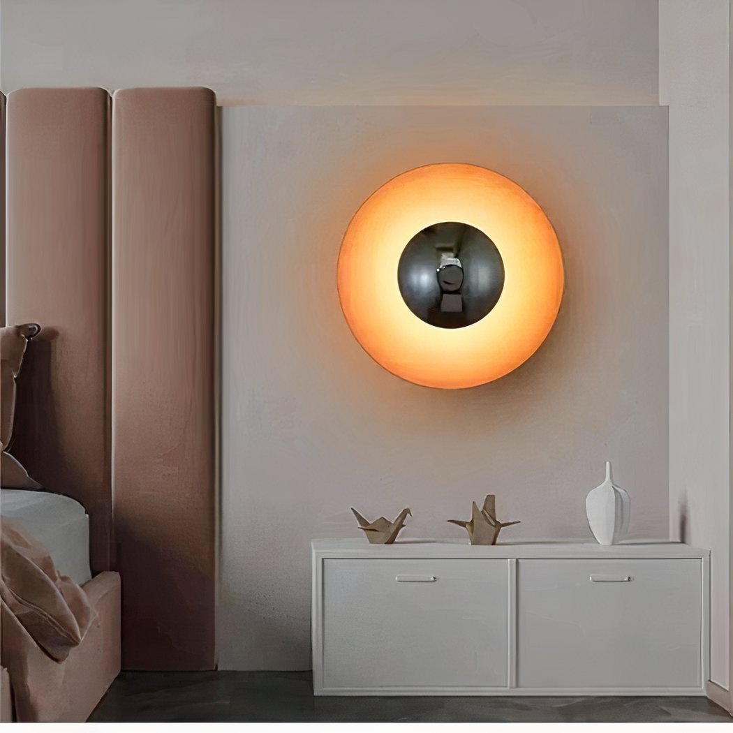 in een slaapkamer met een roze fluwelen hoofdeinde is een ronde wandlamp in vintage oranje stijl te zien
