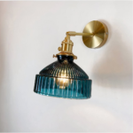 Vintage wandlamp met blauwe glazen kap met groeven en vergulde metalen structuur. Lamp aan, gemonteerd op een witte muur.