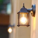 een lantaarnvormige buitenwandlamp brandt op een buitenmuur