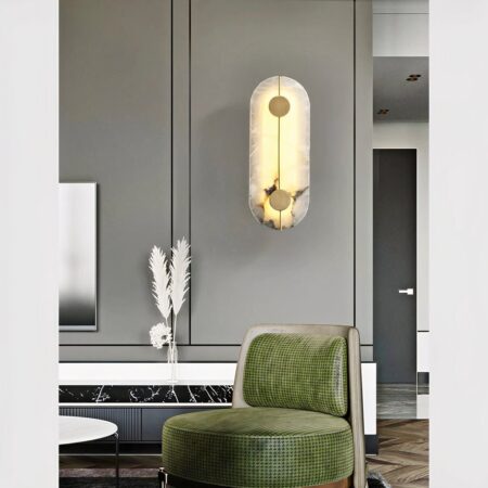 Wandlamp in natuurlijk marmer en messing opgehangen aan de grijze muur van een woonkamer en geplaatst boven een bosgroene fauteuil.