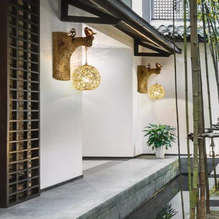 Rieten wandlamp met kleine vogels op een tak gemonteerd op een witte muur en verlicht.