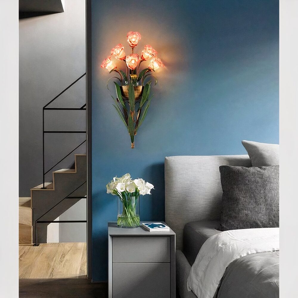 Smeedijzeren wandlamp boeket bloemen in zijn roze versie, verlicht en bevestigd op een eend blauwe slaapkamermuur, naast een bed.