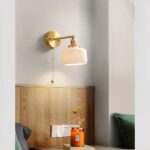 Retro wandlamp van keramiek met lichtketting, in de vierkante bolversie met afgeronde hoeken, verlicht en bevestigd aan een slaapkamermuur.