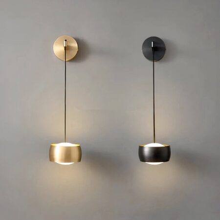 Designer wandlamp in zwart of goud messing, verlicht en bevestigd aan een grijze muur.